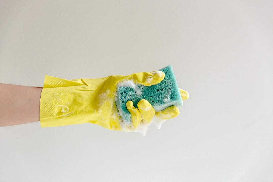 Womans hand with a yellow cleaning glove squeezing a sponge